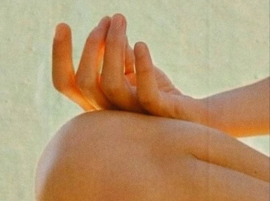 a hand in a mudra rests gently on a bend knee in a meditation position