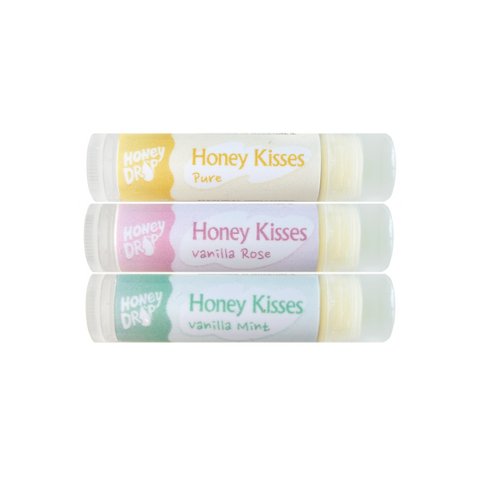 Three Honey Drops Honey Kisses Pure lip balm tubes stacked vertically on a white background, featuring yellow, pink, and green labels with vanilla rose and vanilla mint flavors.