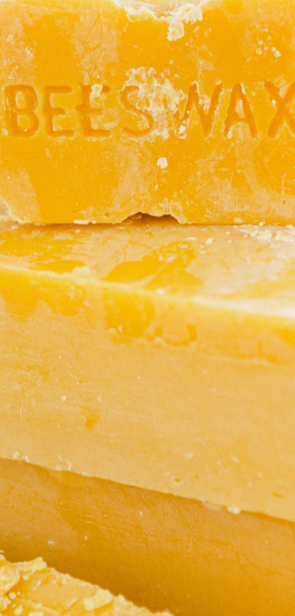 Close-up of thick, textured yellow beeswax bars stacked together, with embossed text partially visible on the top bar.