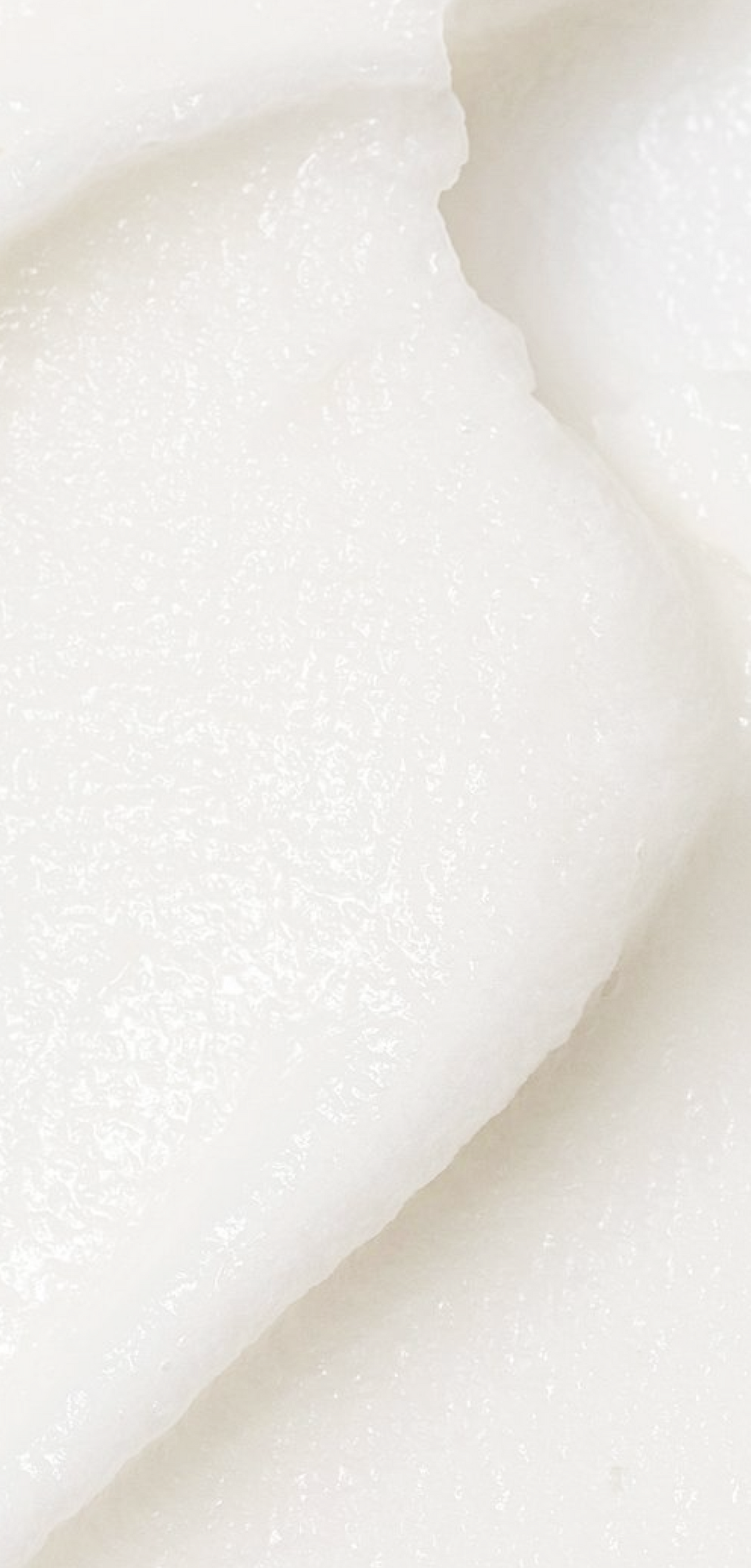 A close-up texture shot of a thick, creamy white cosmetic balm or solid lotion with a soft, slightly granular surface.