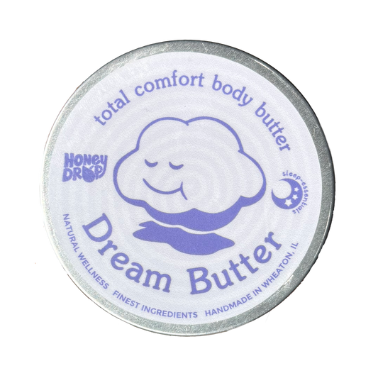 A round tin of Honey Drop Dream Butter body butter with a white lid featuring a purple cartoon cloud and silver metal rim, isolated on a white background.