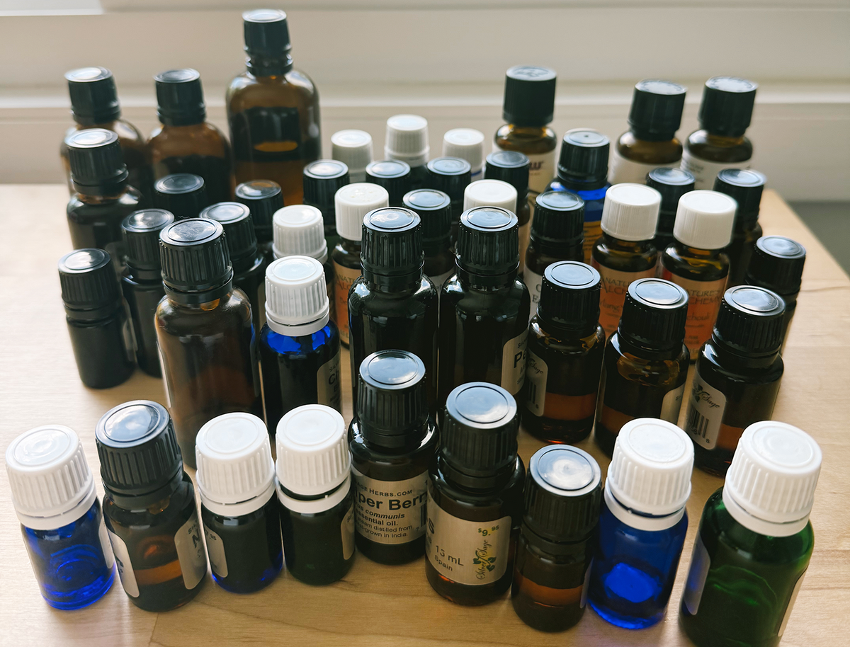 A large collection of small essential oil bottles in amber and dark glass with black and white caps, arranged on a light wooden table.