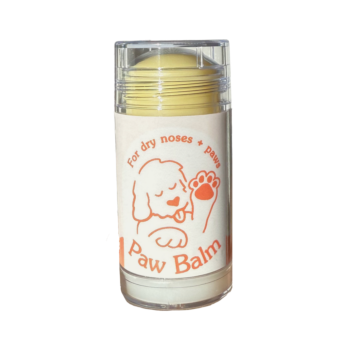 A clear cylindrical container of Paw Balm with a white label featuring an orange cartoon dog and the text 'For dry noses + paw balm' and 'Paw Balm'. The balm inside is pale yellow, and the product is photographed on a clean white background.