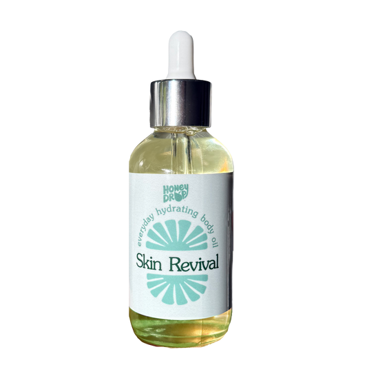 A glass dropper bottle of HoneyDrop Skin Revival everyday hydrating body oil, containing a pale yellow oil, with a white label and silver dropper cap on a white background.